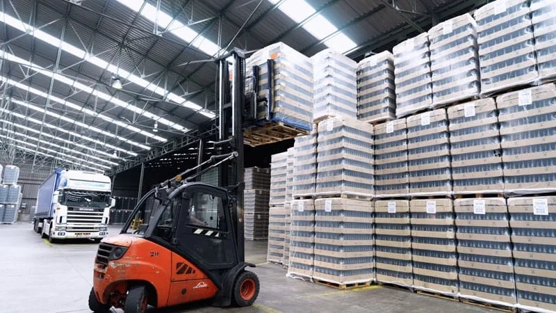 Carretilla elevadora y palés de botellas apilados hasta el techo en un almacén de Vidrala