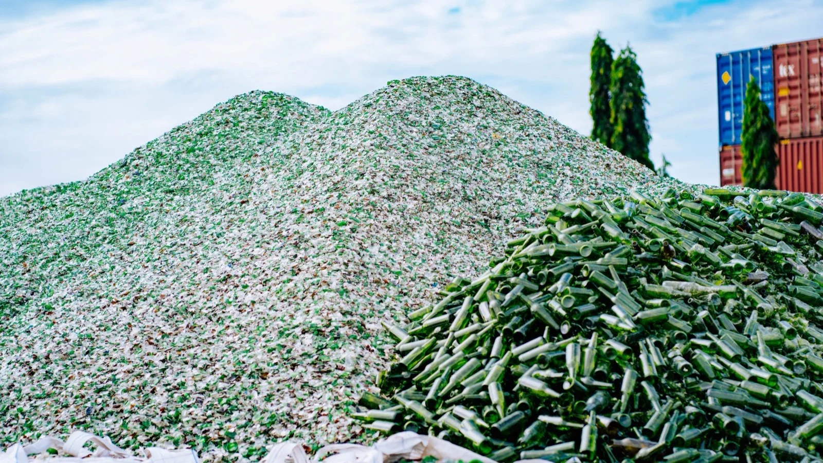 Montaña de vidrio reciclado triturado en una planta de reciclaje, con contenedores al fondo