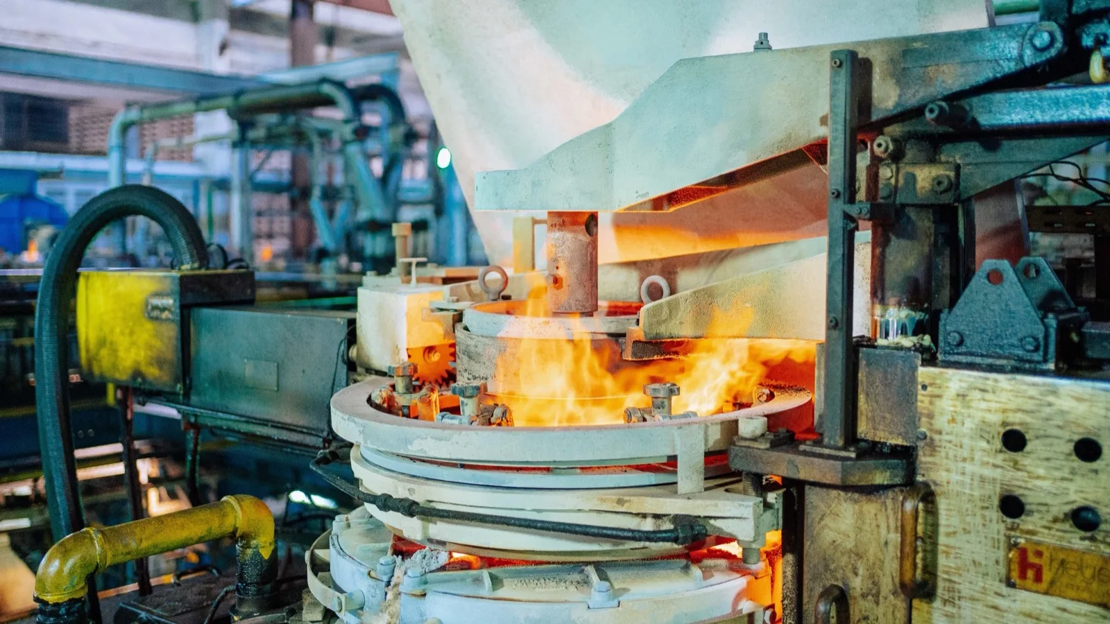 Boca de un horno de vidrio al rojo en una fábrica, con maquinaria industrial alrededor