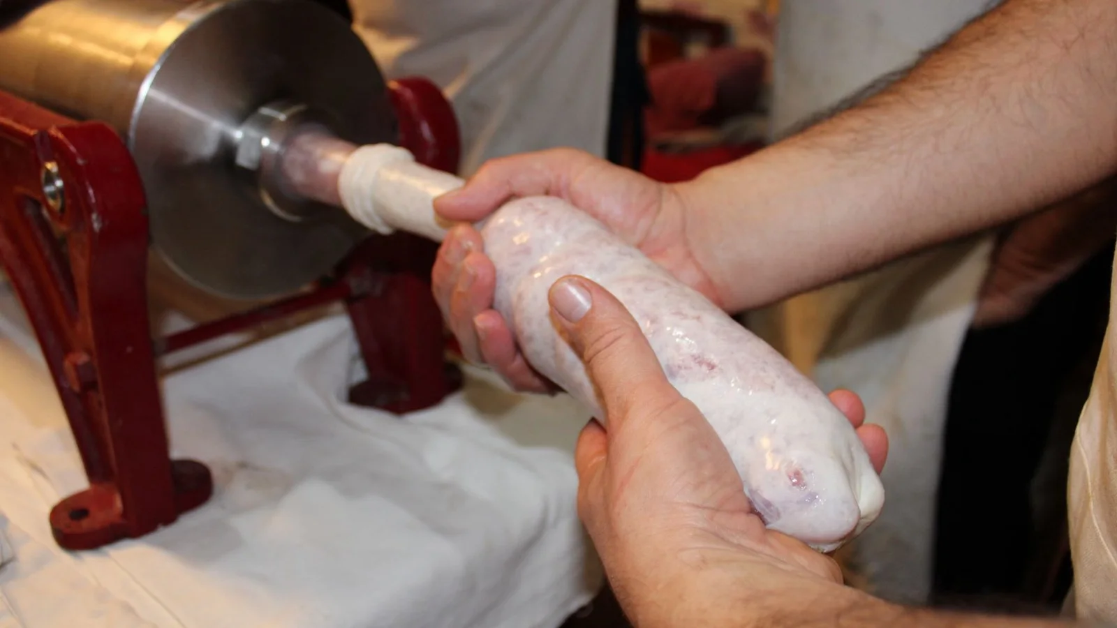 Manos sujetando una pieza de embutido recién formada a la salida de una embutidora de acero